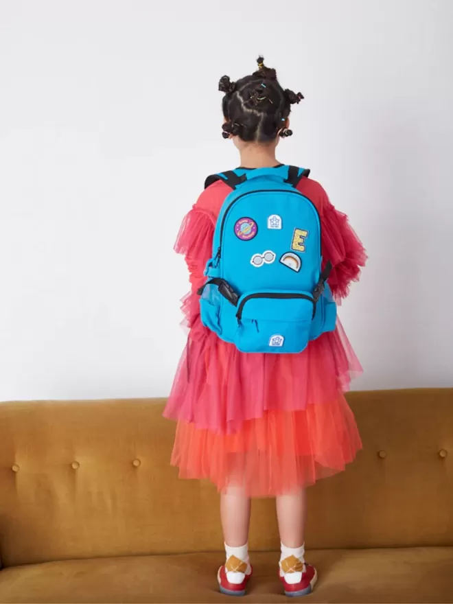 Kid in a pink dress wearing a blue Beltbackpack covered with Pachee patches.