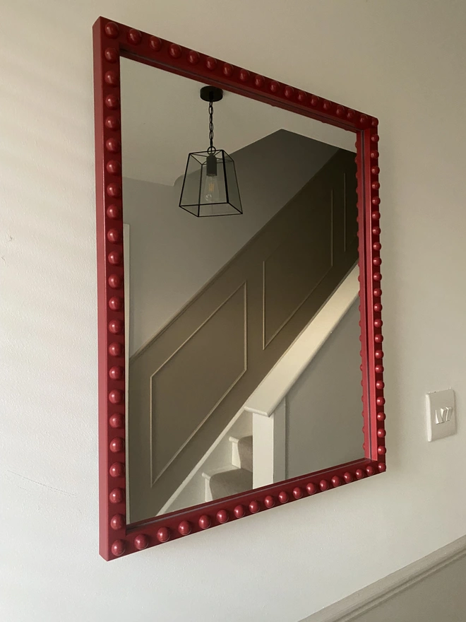 Burgundy rectangular bobbin mirror, shown on an angle, hung in a hallway.