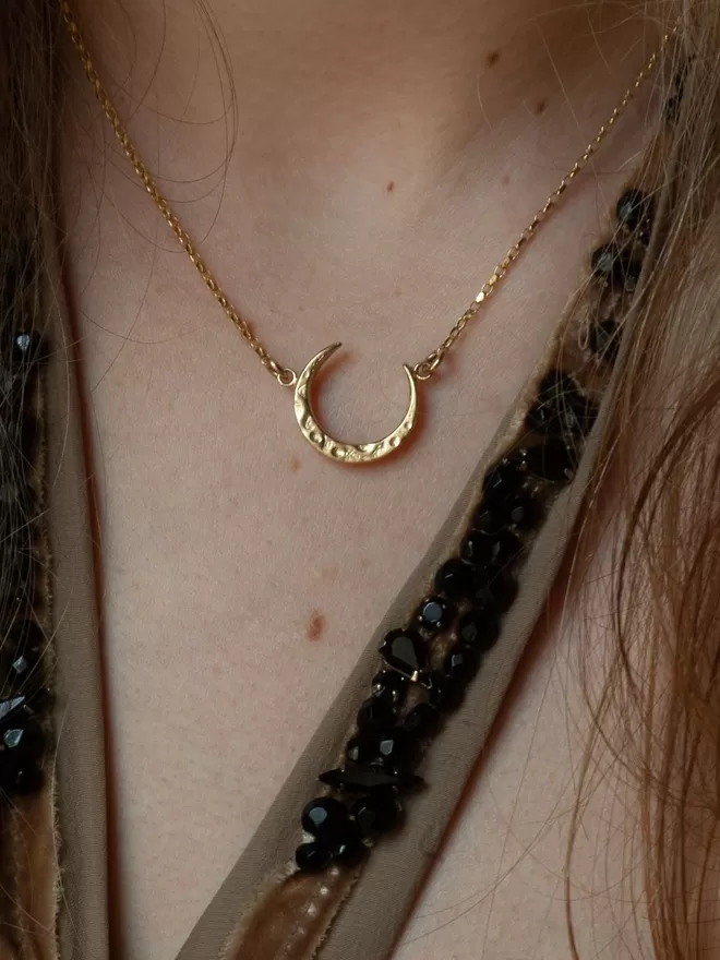 Gold half Moon necklace seen on a woman wearing a halterneck top.