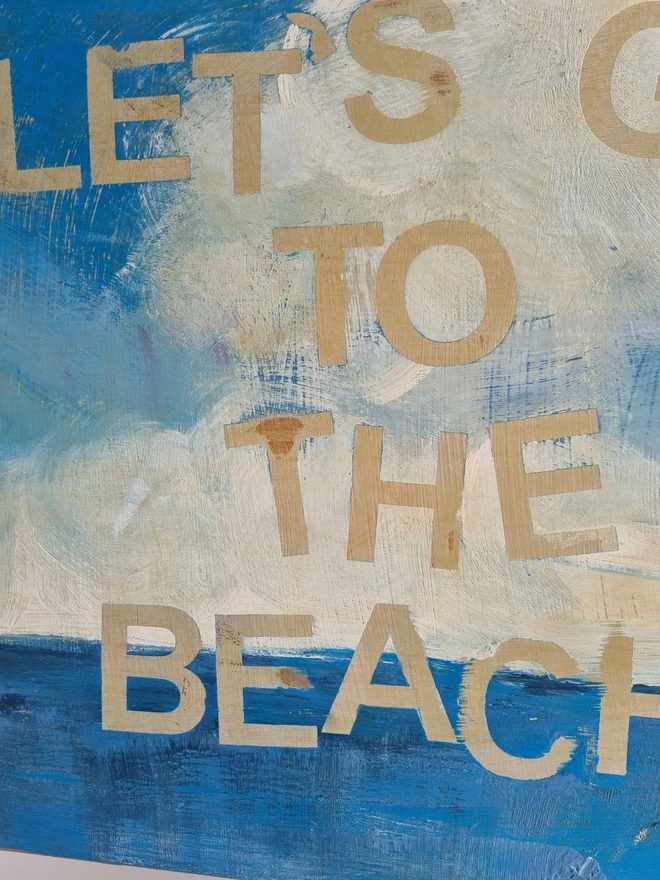 Upcycled art panel in blues and creams featuring a seascape and an image of a retro pin-up lady on a boat and the text reads ‘let’s go to the beach’ in a distressed, shabby chic style