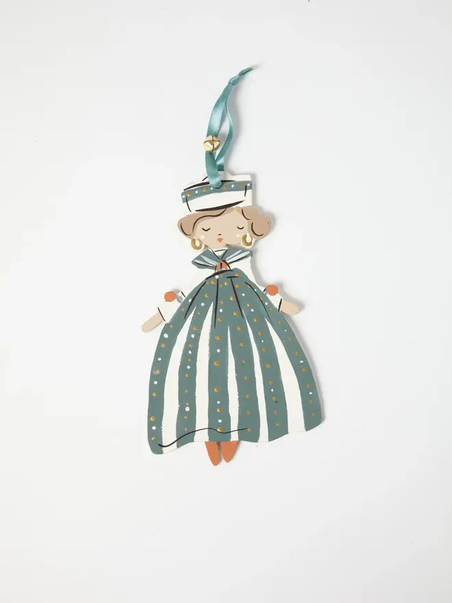 Sailor Queen Tree Dancer. a flat lay product shot of the sailor queen tree dancer hanging ornament on a plain white background, showing a figure with curled hair and gold hoop earrings, wearing a striped sailor hat and a teal and cream striped gown dotted with gold. she hangs from a teal ribbon with a small gold bell attached, her orange-toned shoes peeking out beneath the full skirt. hand-painted detailing gives the ornament a folk-art, storybook charm.