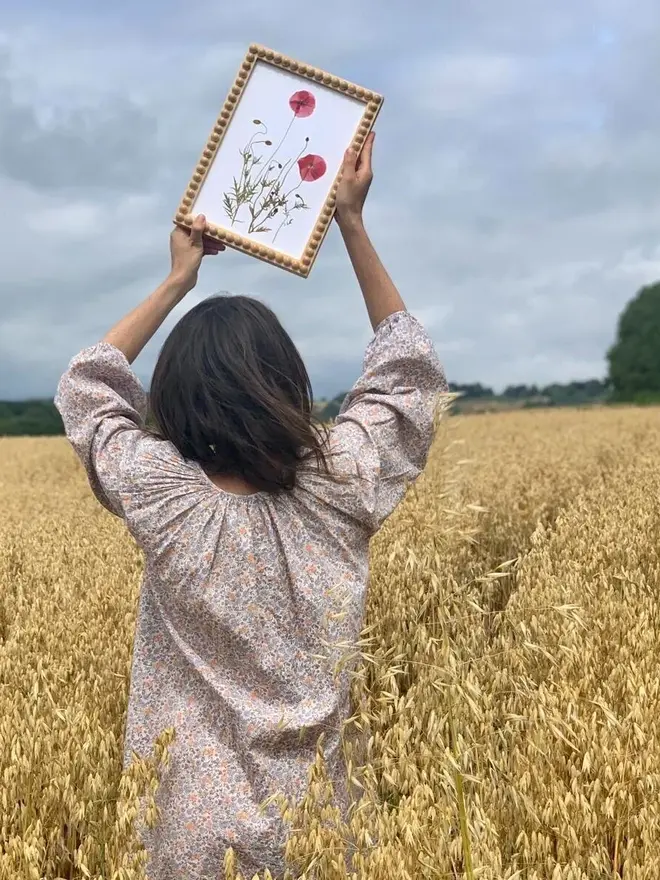 Pressed Field Poppy Print, a woman holding a poppy print in a field. 