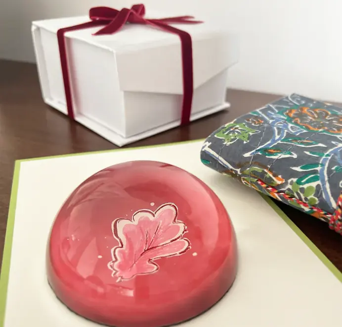 Round pink oak leafpaper weights on a wooden table beside a wrapped present. 