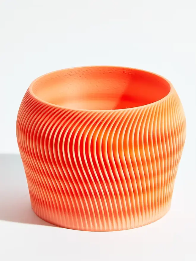Sustainable 3D Printed Coral Orange Plant Pot, orbital design against a white background.