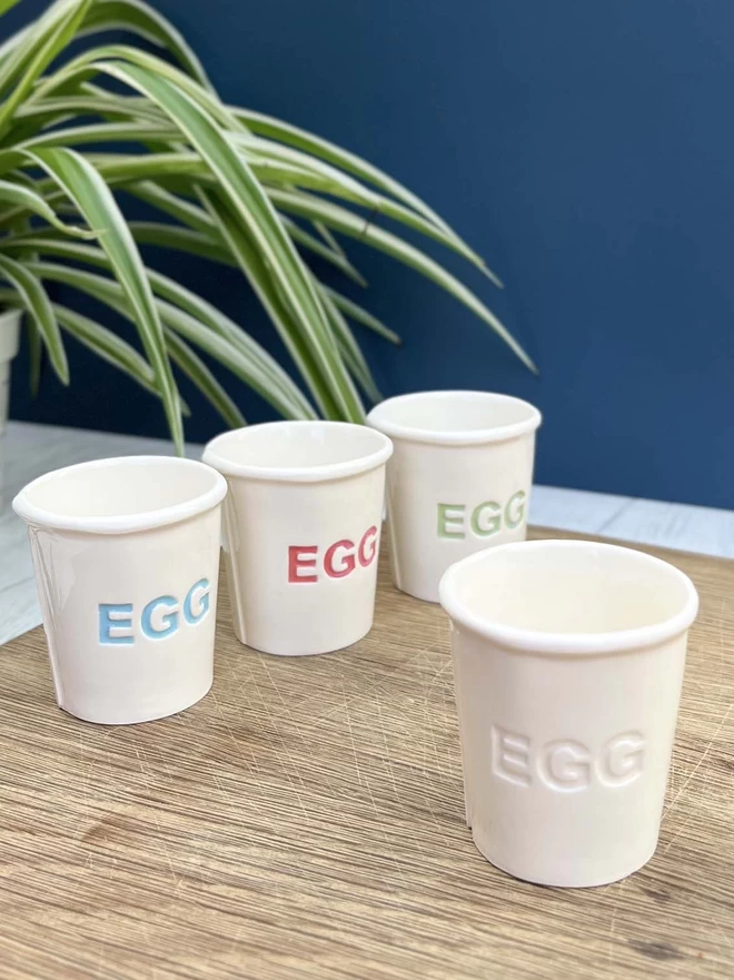 4 handmade egg cups showing the different colours the lettering can be in- blue, red, green or plain.