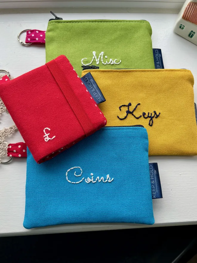 Set of 3 colour coin purses and 1 red card wallet laid on a while windowsill