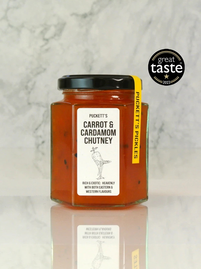 carrot and cardamom chutney. a jar of chutney photographed on a marble background.