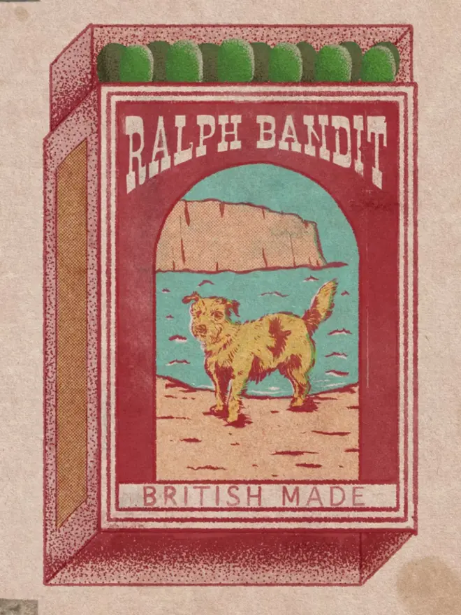 An illustrated, retro-style matchbox with a dark red background and a brown, textured border. The central image shows a scruffy, spotted dog standing on a beach. Behind the dog is a large, brown cliff and a body of water with a turquoise sky. A banner at the top reads "RALPH BANDIT," and a banner at the bottom says "BRITISH MADE." The match tips on the top are dark green circles. The image has a very grainy, vintage texture.