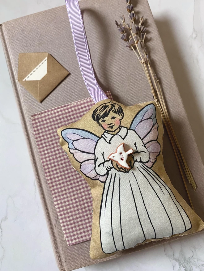 a boy tooth fairy decoration holding a peace white dove potterny button with a lilac ribbon for hanging