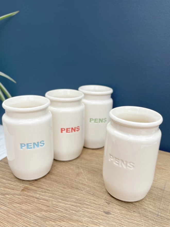  4 handmade pots showing the different colours that the word ‘pens’ can be in - blue, red, green or plain