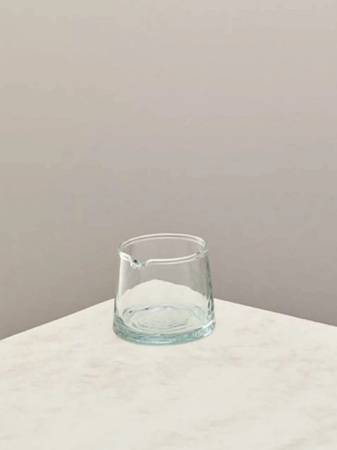 Low Jug, a small glass jug sitting on a counter top against a plain backdrop. 