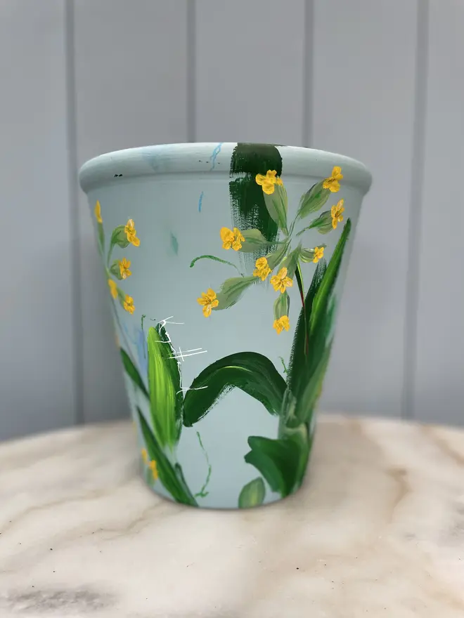 Unique hand-painted terracotta pot featuring yellow cowslip flowers on a pale blue background