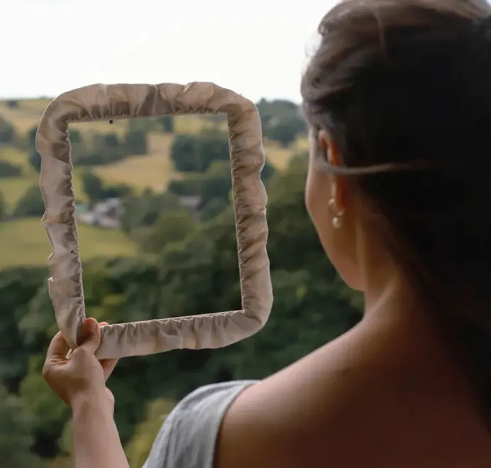 Soft ruffled frames with off white fabric trim being held near mountains. 