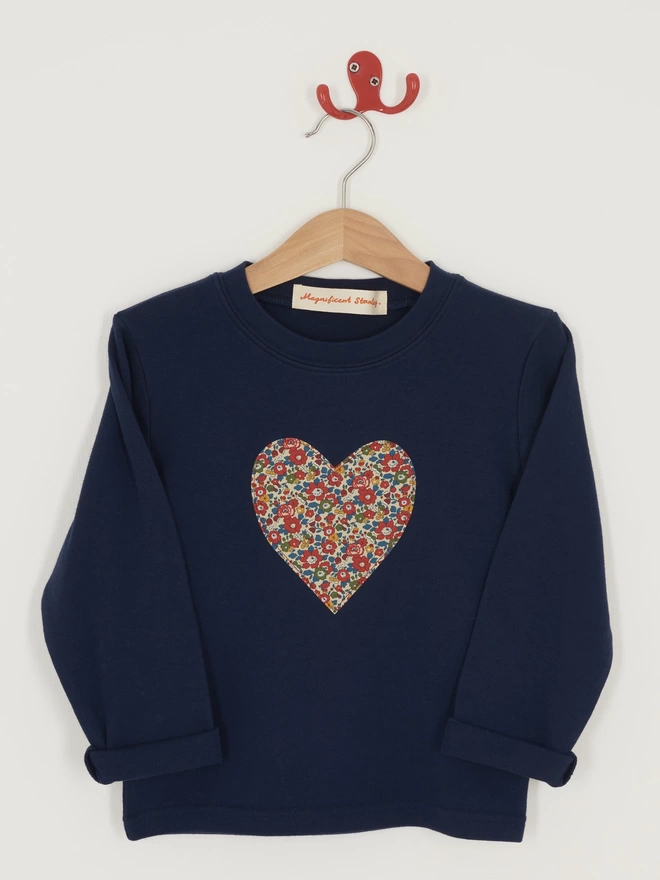 a long sleeve navy t-shirt with a liberty floral heart on the front, hanging on a hanger