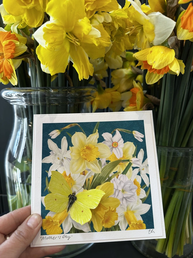 A close up photo of a Butterflygram card being held. The photo shows the floral background of daffodils and narcissi and a yellow, three dimensional butterfly sits on the flowers. The card personalised with a hand written name in the bottom, left corner.