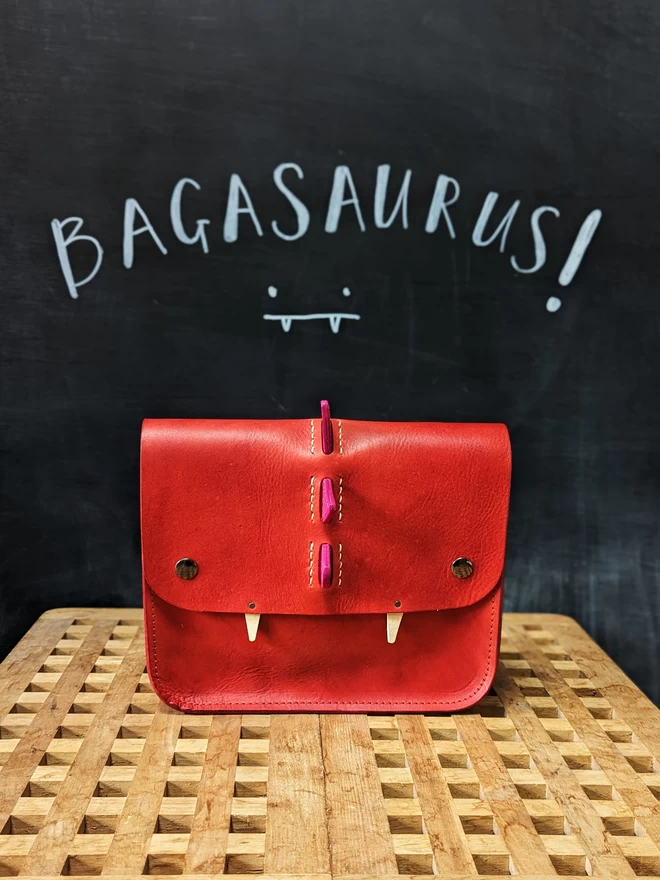 Front view of red, hand- dyed leather 'Bagasaurus' backpack with pink spikes and pointed white fangs