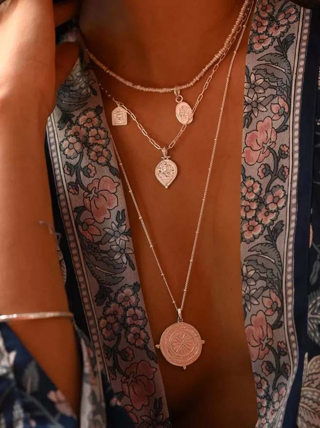 Long silver coin pendant worn with smaller boho layering necklaces with model wearing navy blue printed kimono