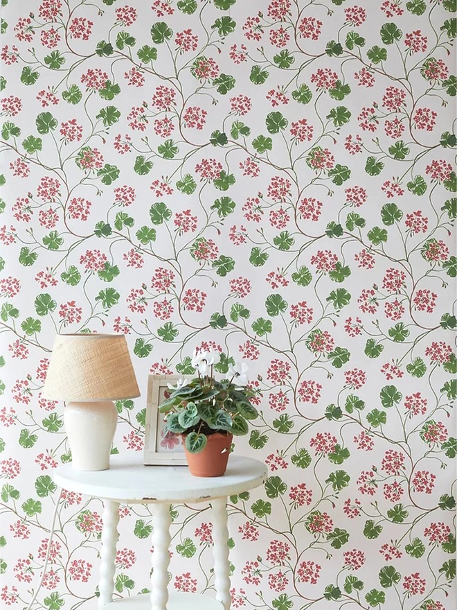 Geranium wallpaper in a beautiful room with white side table with pot plant and lamp