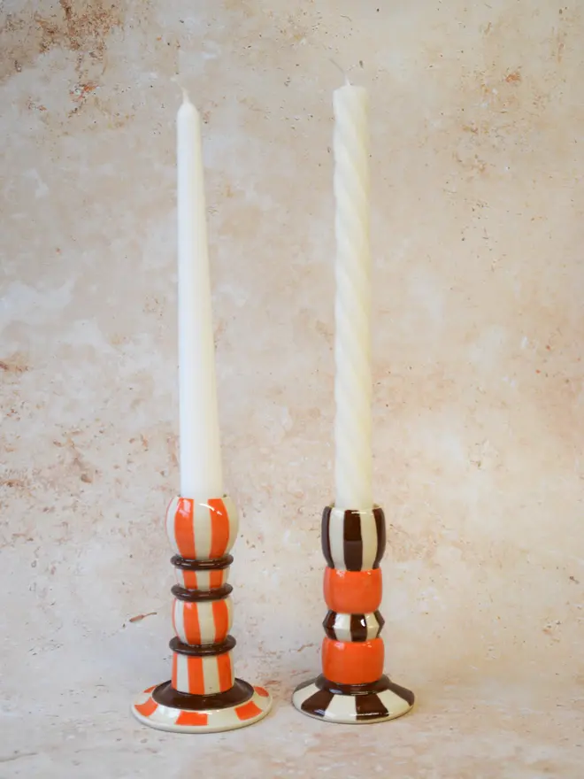 Handmade striped ceramic candlestick holders - brown and orange pairs displayed with taper candles