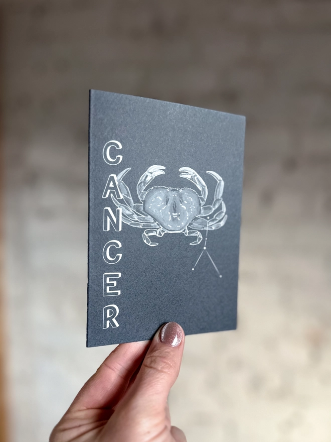 a greetings card featuring a greyscale illustration of a zodiac style crab with the text “CANCER”
