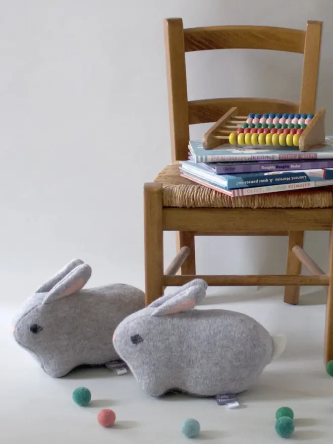 two plush grey bunnies next to a wooden chair with books and toys