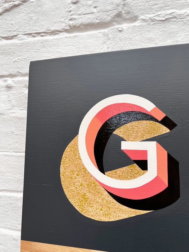 Close up of letter G from GROW hand painted sign in coral, dark grey and chartreuse, against a white brick wall, at an angle. 