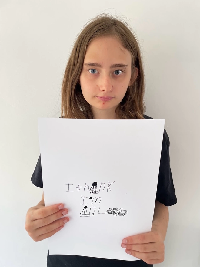 Piper holding her digital print with her unique black ink writing on a white background