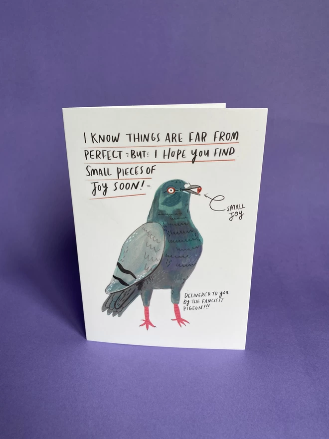 An illustrated A6 Greeting card with a pigeon with a tiny heart in their beak that reads - I know things are far from perfect but I hope you find some pieces of small joy soon!