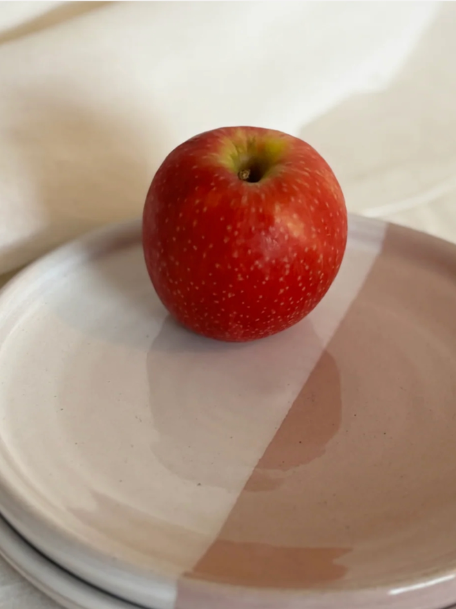 Side Plate. A stack of pink and white side plates topped with a red apple, set against a clean, simple background.