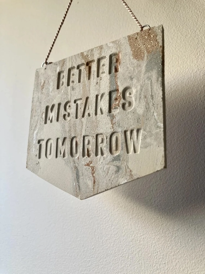 'Better Mistakes Tomorrow' Banner, a clay banner hanging against a plain backdrop.