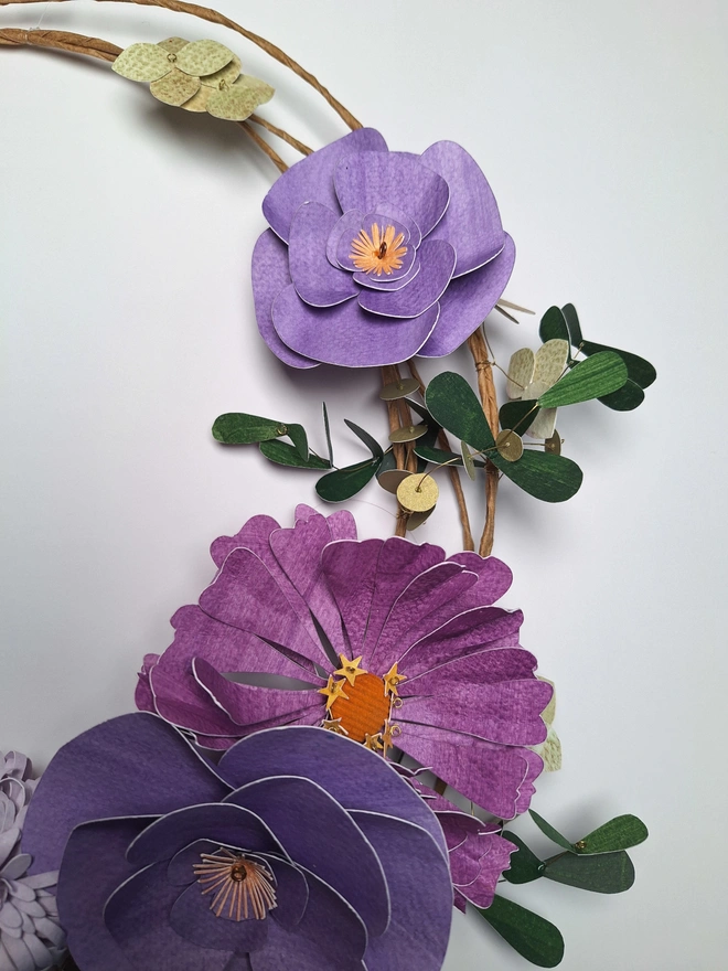 Close up of a small, purple camelia flower and zinnia, accompanied by leafy stems
