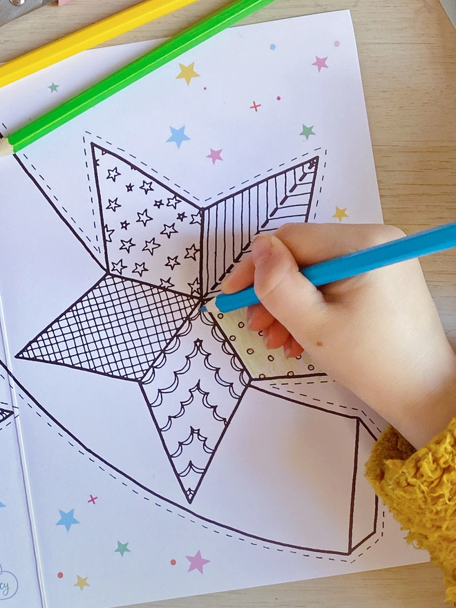 A child is colouring a Christmas greetings card with a star tree topper design.