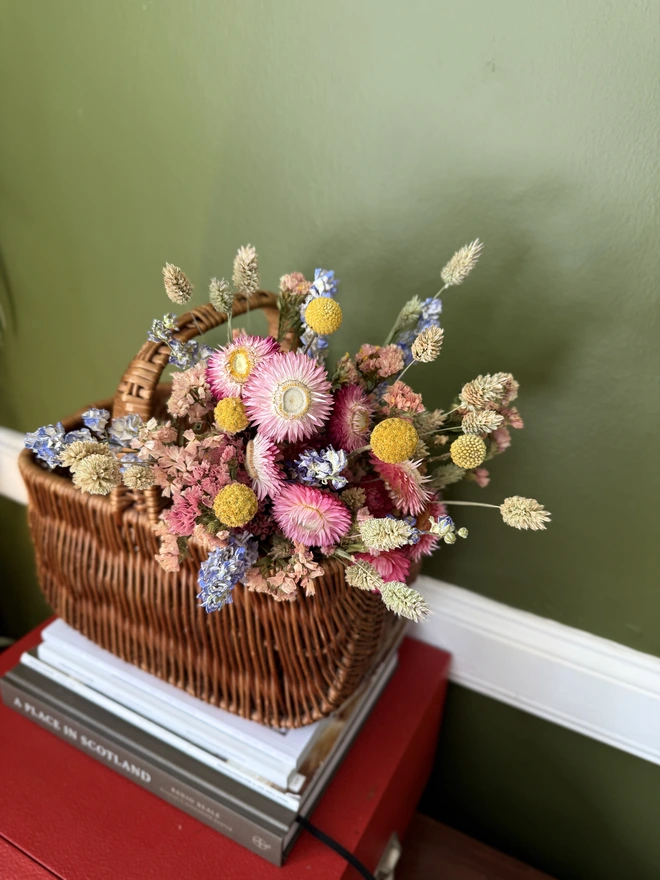 a bouquet of dried flowers in bright colours displayed in a wicker basket against a green wall