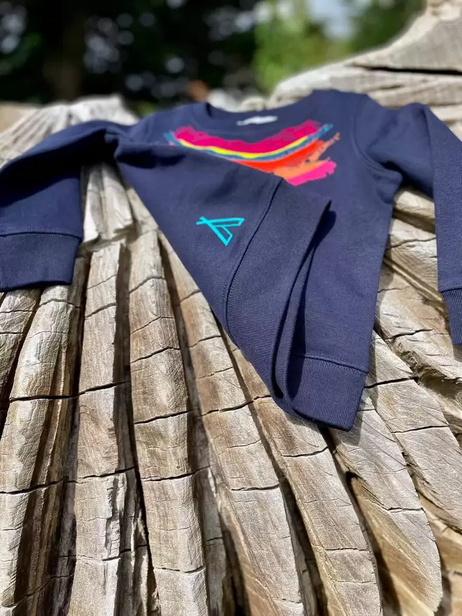 The 'Creator' Children's Printed Sweatshirt lay on a carved log with The Faraway Gang logo visible.
