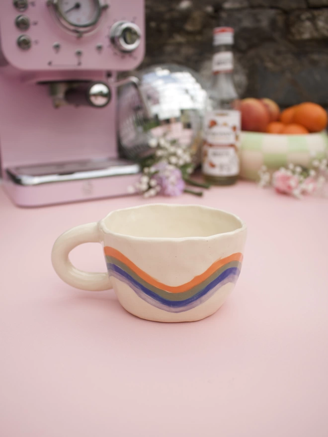 wavey stripes of orange, green, blue and purple around a handmade stoneware pottery mug