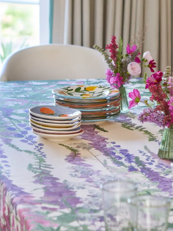 Horatio’s Garden Foxglove Tablecloth. A white tablecloth patterned with purple and green foxgloves.