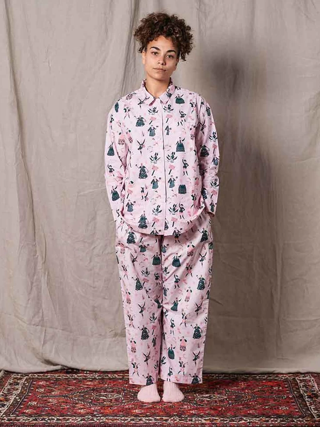 Model is wearing a button up pale pink shirt style pyjama top with featuring our feminist icons and loose fitting bottoms in the same colour with our  icon print
