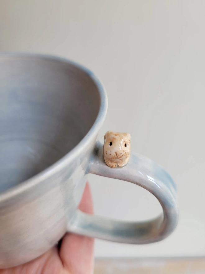 Close up of a tiny beige ceramic bunny rabbit sitting on a grey hand made tea cup 
