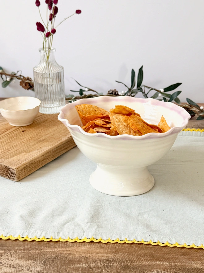 Undulating hand thrown porcelain stem bowls with satin cream glaze with pink rim on a rustic Christmas table top