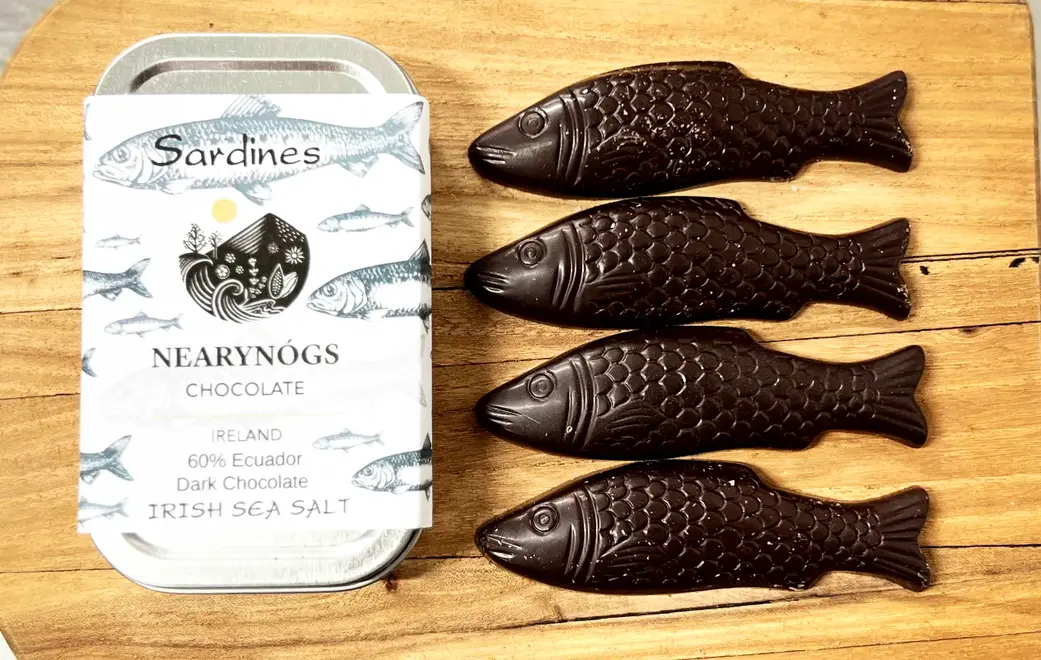 Sardines Dark Chocolate 60% (Tin Of 4), a tin of chocolate fish sitting on a wooden surface. 