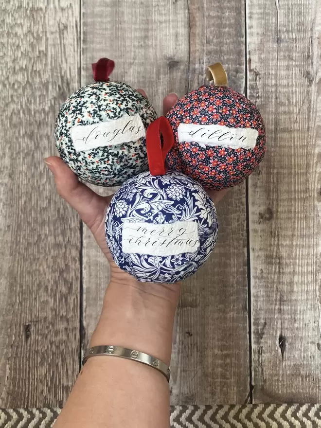 3 personalised baubles with names held in front of a table