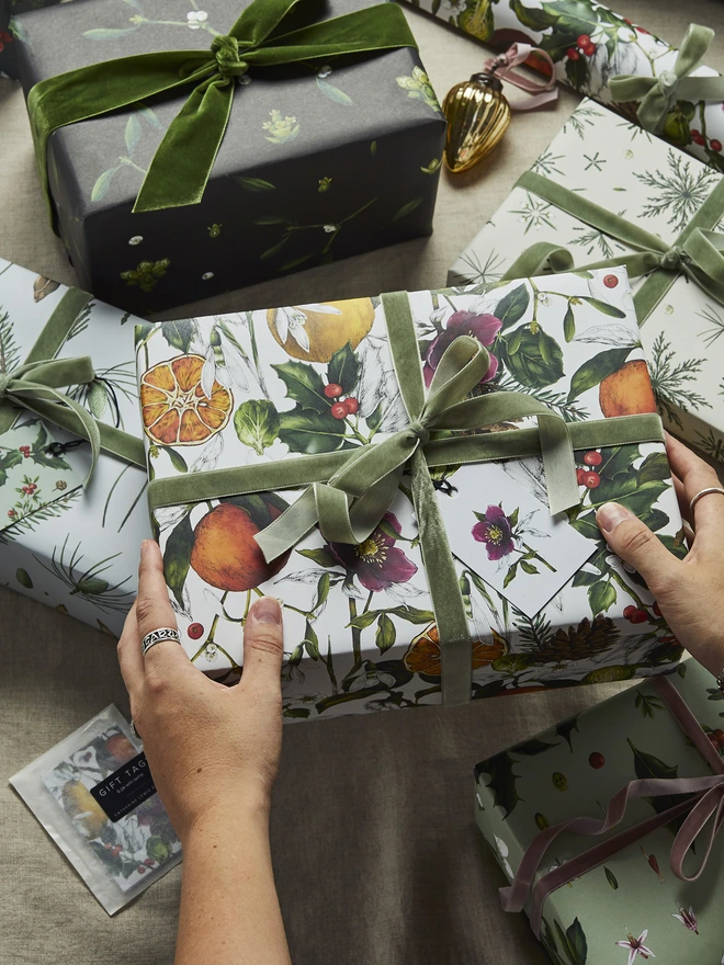 A busy ivory based christmas wrap with festive elements like clementines, holly and hellebores being held