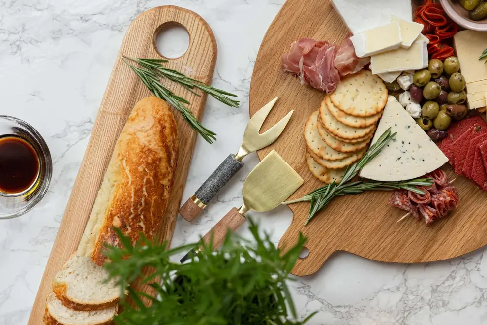Large Oak Oval Serving Board, a wooden serving board sat on a stone surface accompanied by a spread of food. 
