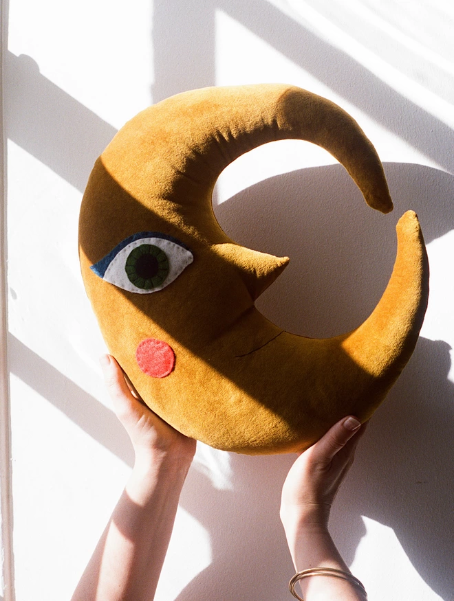 golden moon cushion hel;d up next to a window