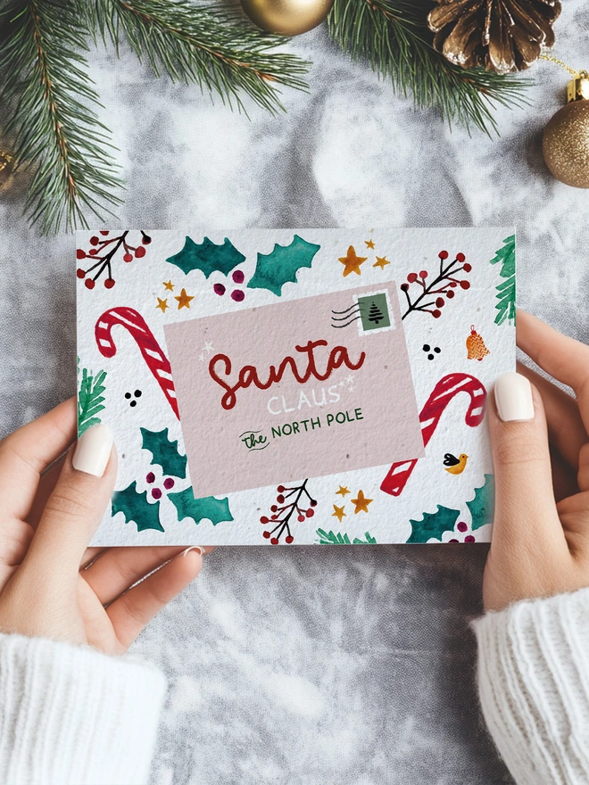 A pair of hands is holding a Christmas card with an illustrated postcard Christmas design. The card is in a Christmassy scene
