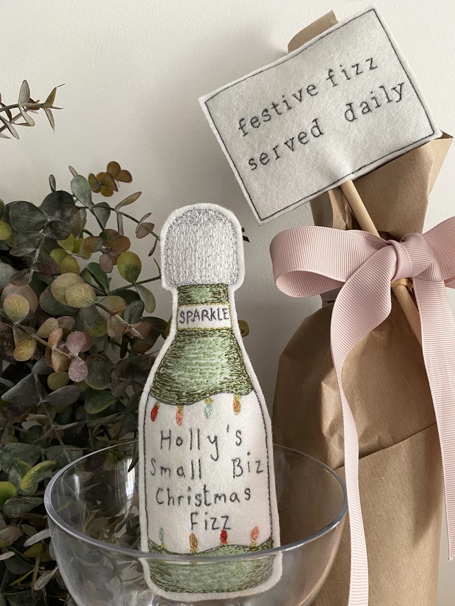 A Little more Christmas Fizz Bottle in a glass with wrapped bottle with festive fizz sign