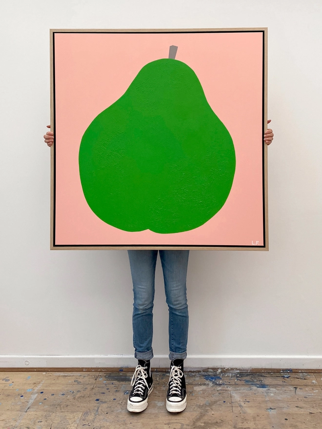 Painting of a giant green pear on pink background with person holding it up from behind so only their legs are visible