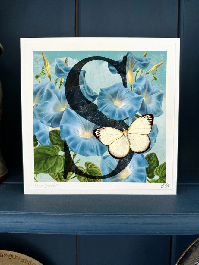 A Personalised Birthday card, with a large letter S for recipient name example, Sarah, It features the September birth flower, Morning Glory, a blue trumpet, climbing flower against a bright blue sky. There is a white 3D papercut butterfly on the letter S. This can be personalised to any letter. 