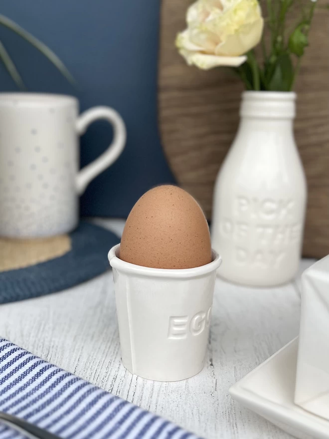 A handmade ceramic egg cup, has the word ‘egg’ recessed in capital letters on its side.