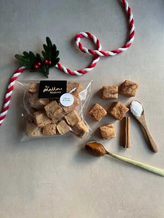 The-Mallow-makers-looking-down-on-packet-of-churro-handmade-marshmallows-with-spoons-of-dulce-de-leche-and-salt-and-cinnamon-stick-with-christmas-ribbon
